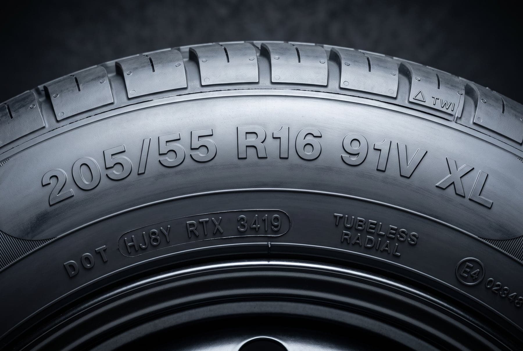 Flanco de un neumático con la medida 205/55 R16 91V XL, el código DOT, el testigo de desgaste TWI y la homologación europea grabados en relieve
